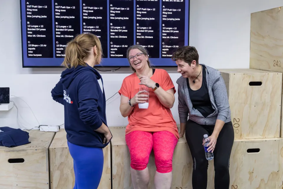Tre kvinder taler og griner sammen ved træningskasser efter bootcamp.